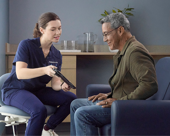 Aspen Dental professional reviewing information on a tablet with an older adult man during a dental consultation.