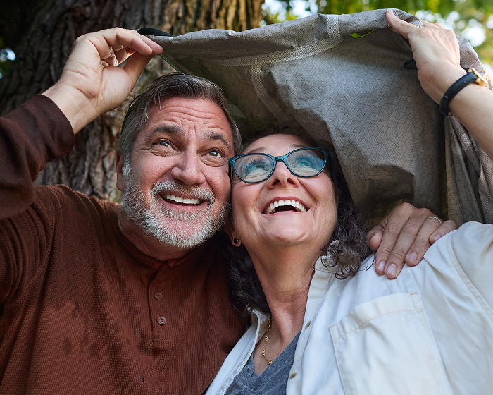 Smiling couple holding a jacket over their heads outdoors.