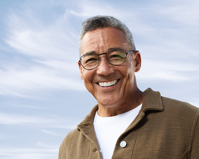 Alt text:
Smiling older adult man wearing glasses outdoors with a confident expression.