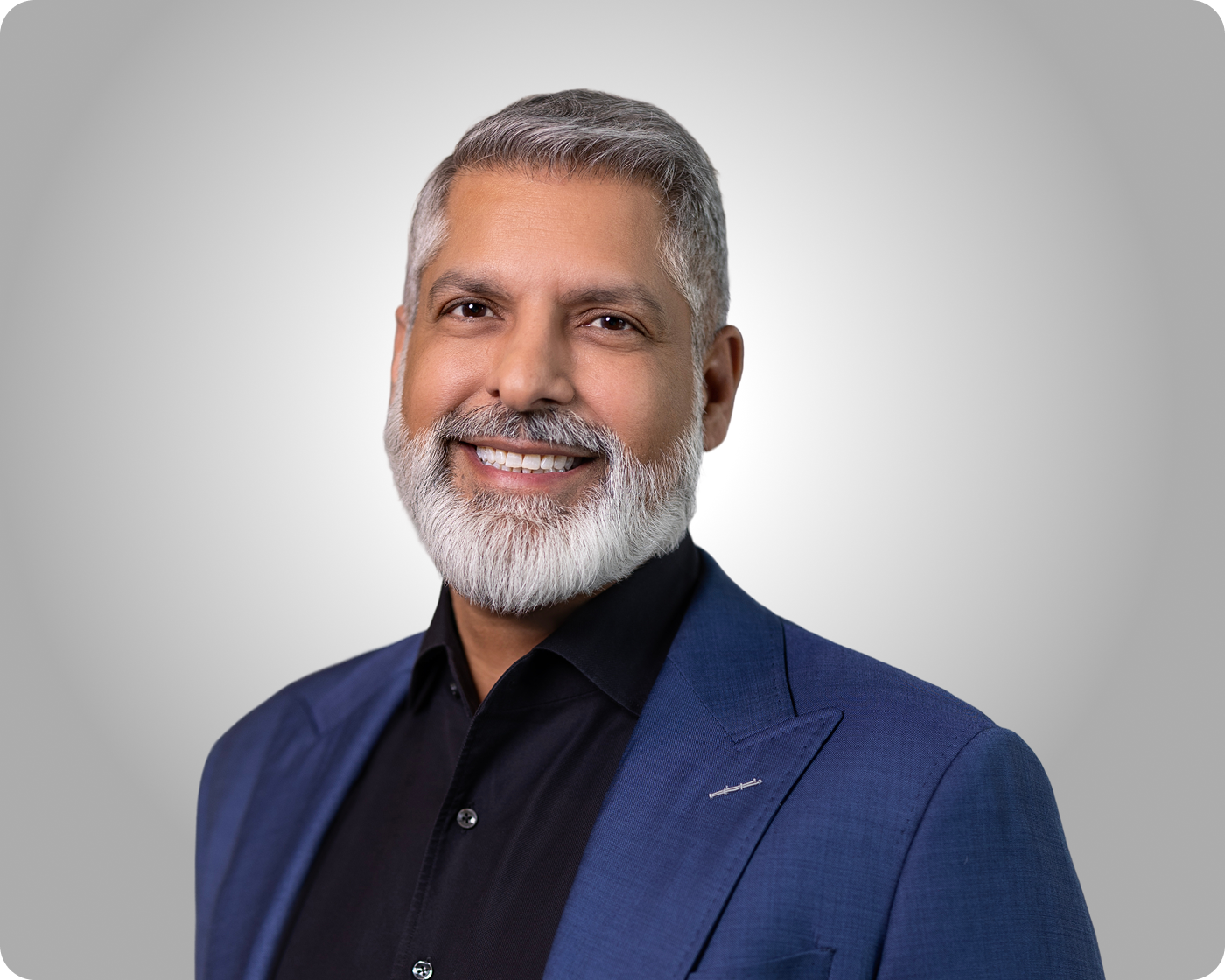 Professional headshot of a smiling man with gray beard wearing a blue blazer against a gray background