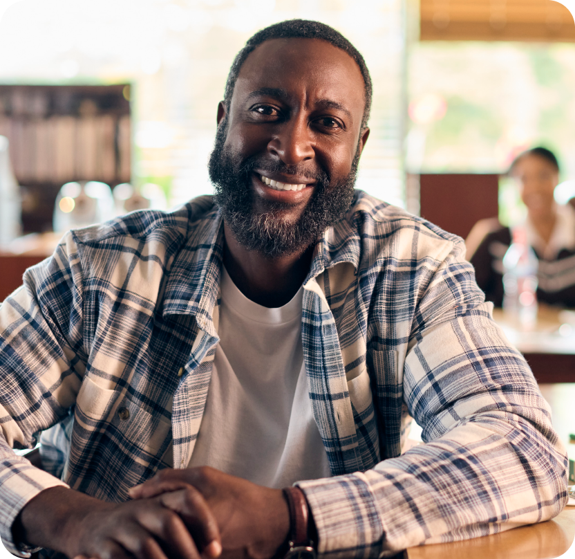 Smiling man sitting at a café table, looking at the camera.
