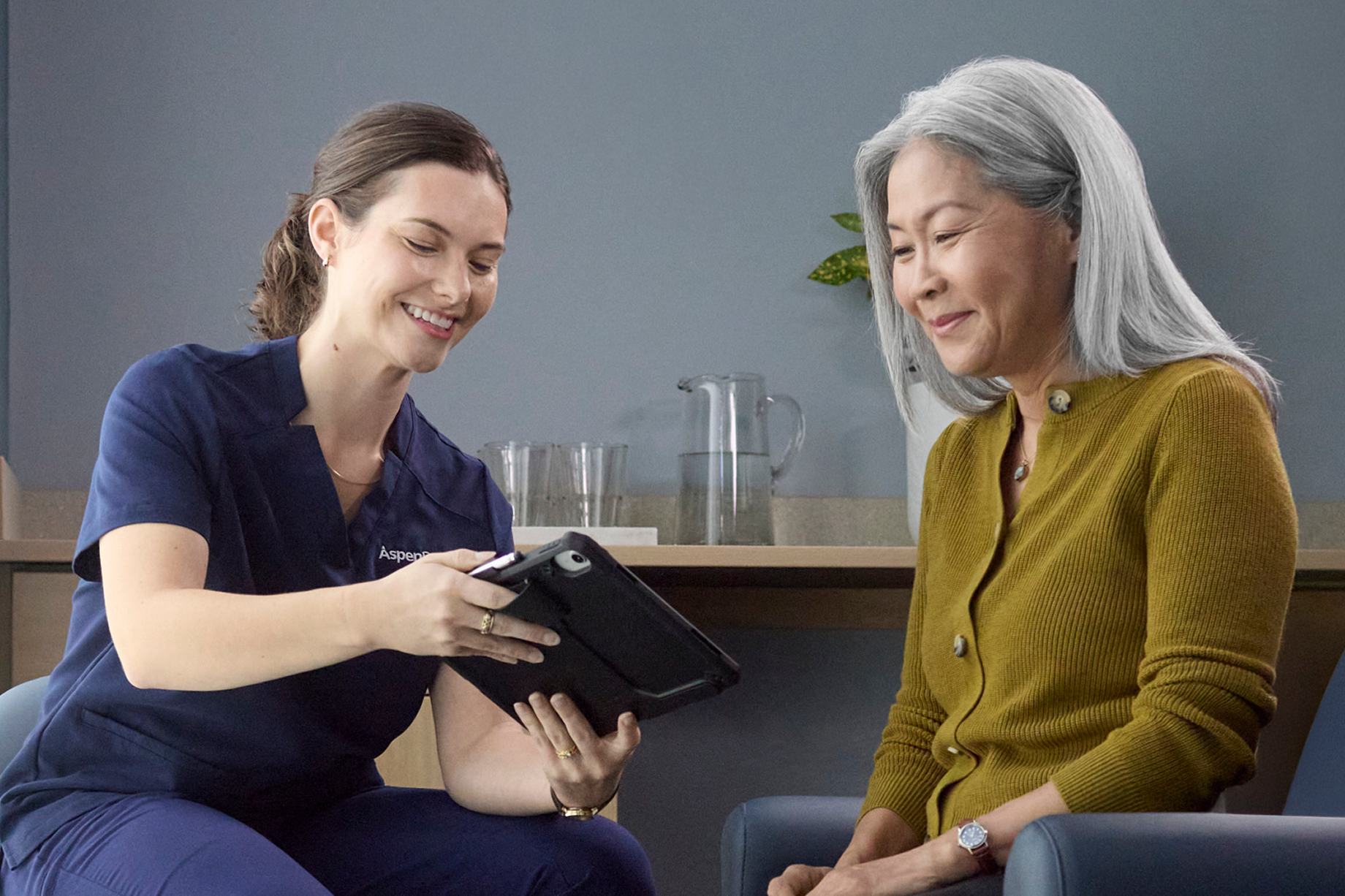 Dental professional reviewing information on a tablet with an older woman during a dental consultation.