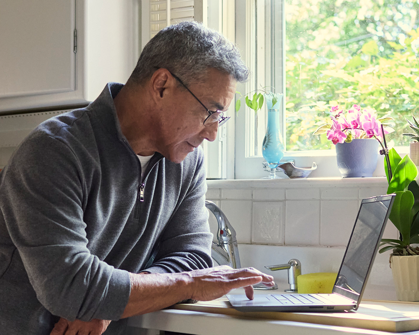Older adult man using a laptop at home, researching or managing dental care information.