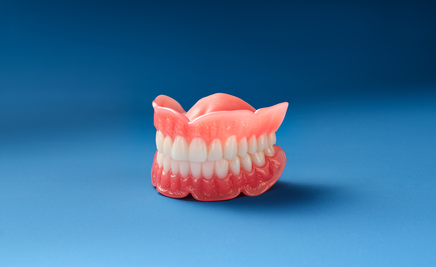 Full upper and lower denture model with pink gum base displayed on a blue background.