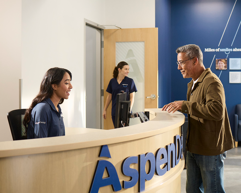 Alt text:
Patient speaking with an Aspen Dental team member at the front desk during check-in.