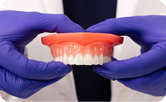 Dental professional holding a denture with both hands.
