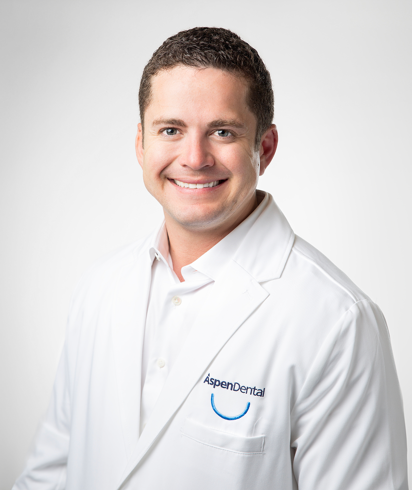 alt text text: Headshot of Dr. De La Rosa, an Aspen Dental dentist, smiling in his white lab coat.