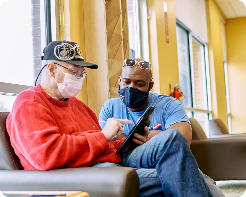 Two masked men, one older and one younger, engage with a tablet together