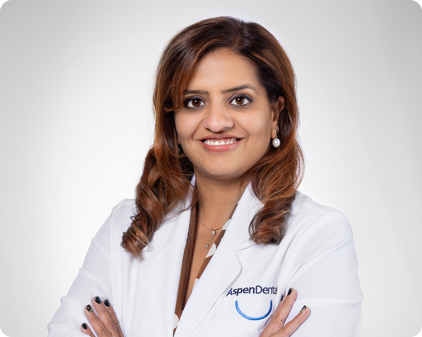 Professional headshot of a smiling female dental provider wearing a white coat against a gray background