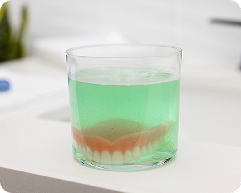 Denture soaking in a glass of cleaning solution.