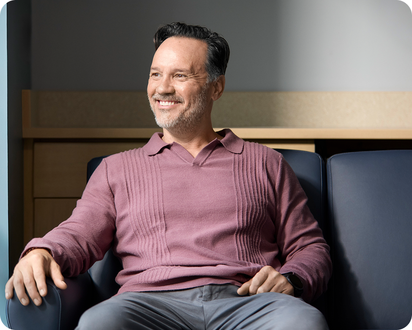 Alt text:
Smiling man seated indoors with a relaxed expression.