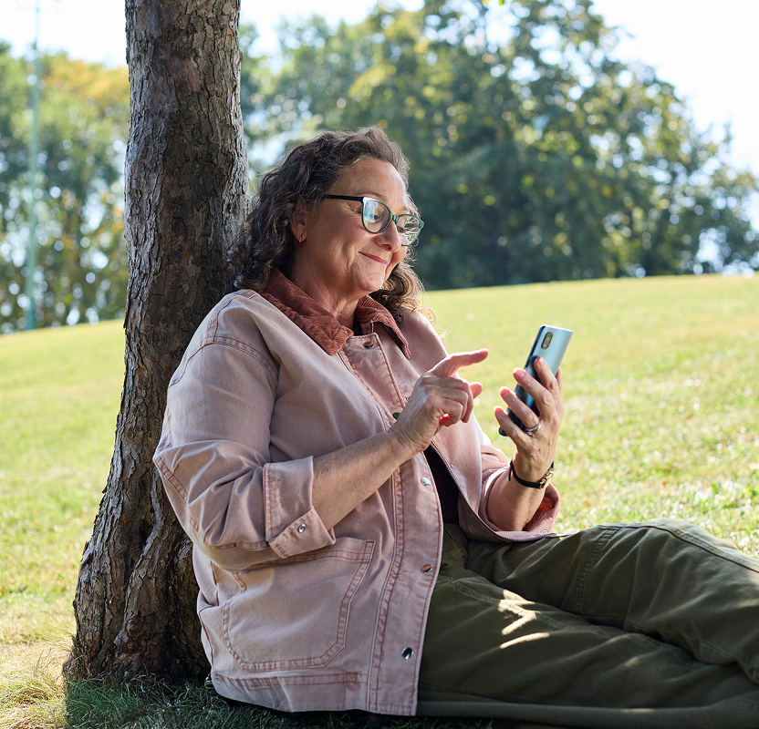 Woman sitting under a tree outdoors using a smartphone.