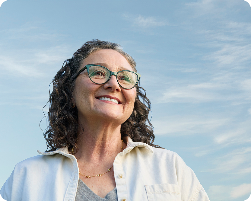 Alt text:
Smiling woman wearing glasses outdoors with a confident expression.