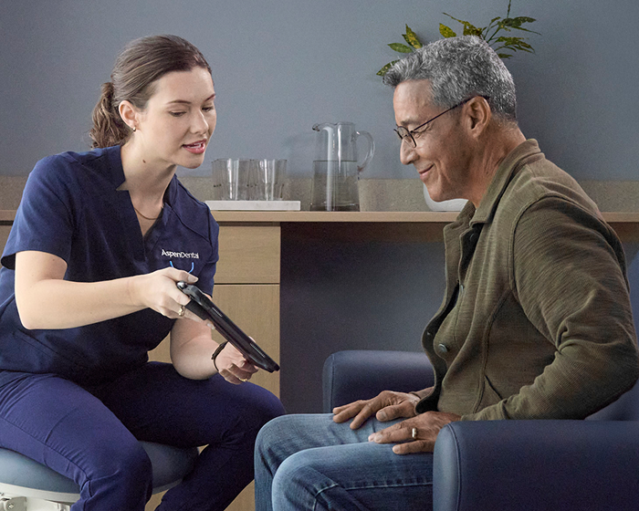 Aspen Dental professional reviewing information on a tablet with an older adult man during a dental checkup.