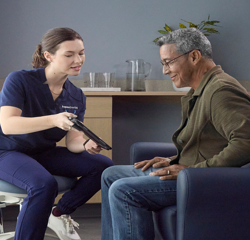 Aspen Dental professional reviewing information on a tablet with an older adult man during a consultation.