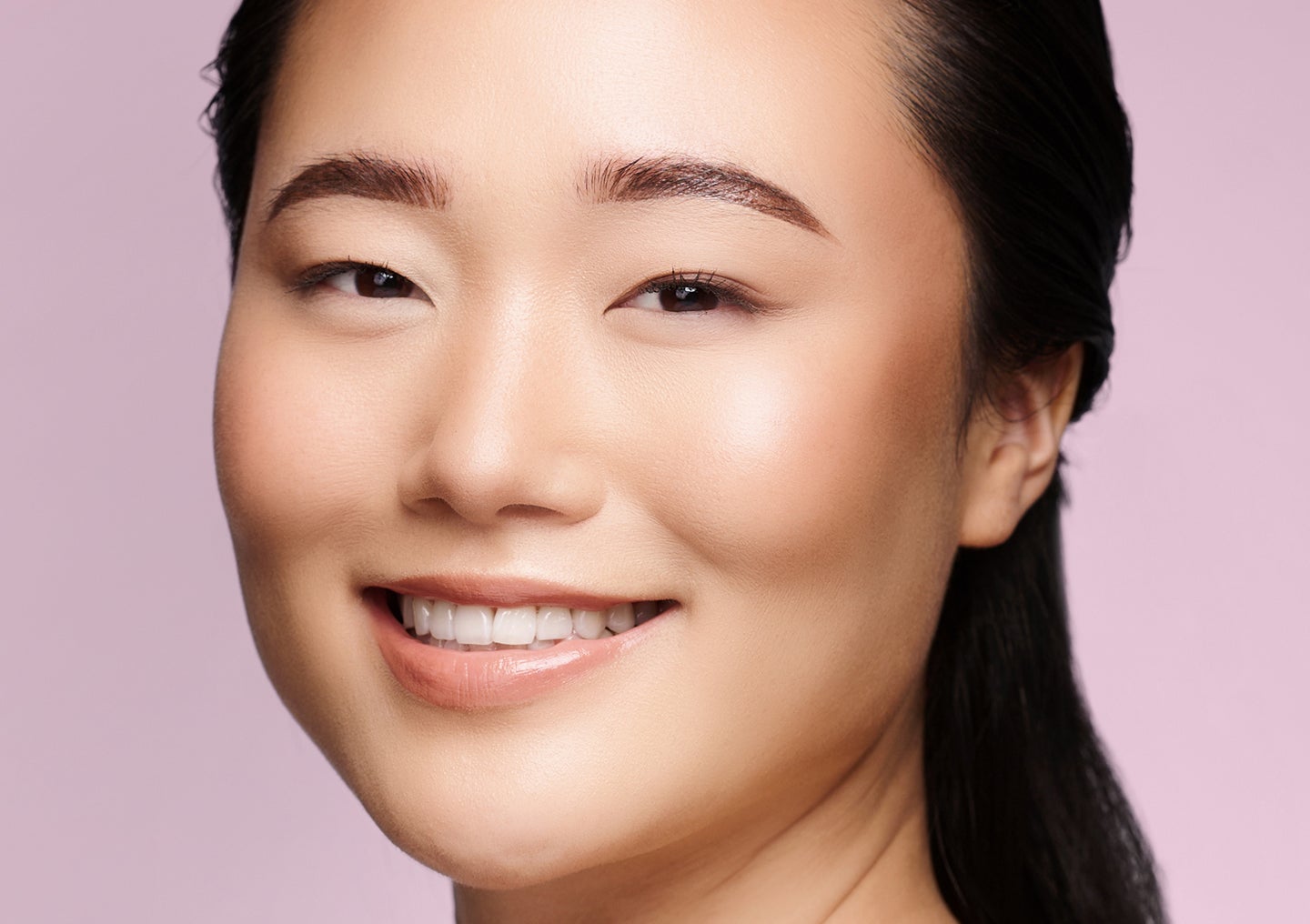 A woman with radiant, smooth skin smiles against a lavender background