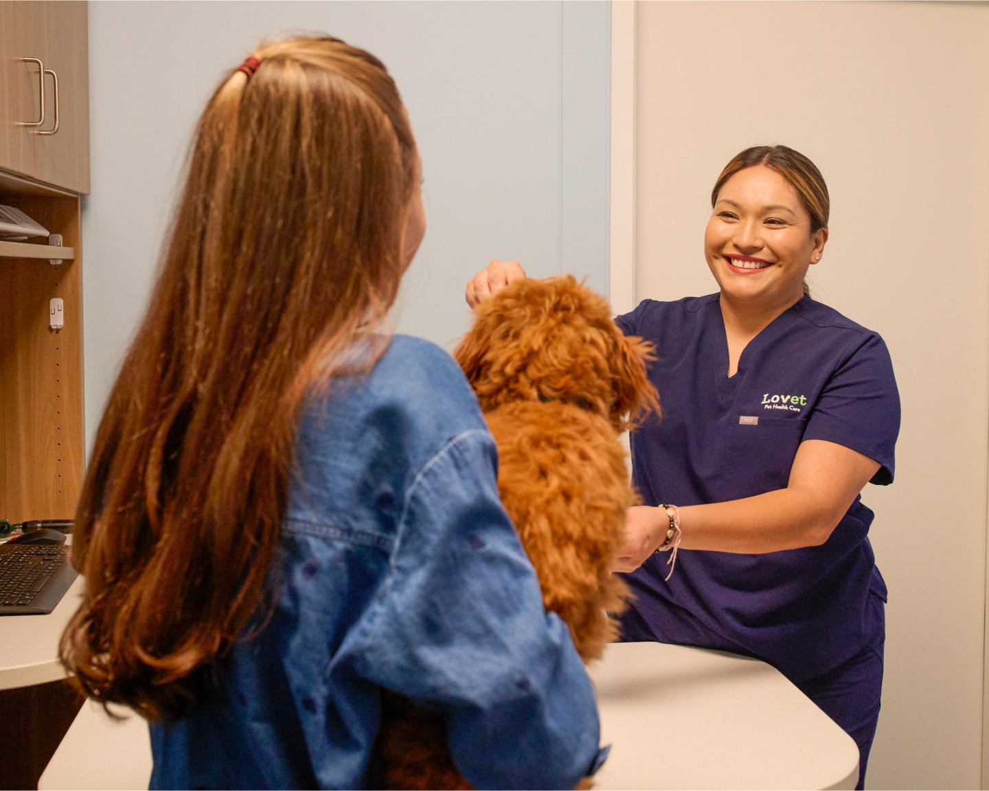 An out-of-focus pet parent and their Golden Doodle from behind in the foreground, with a Lovet team member smiling and in focus in the background.