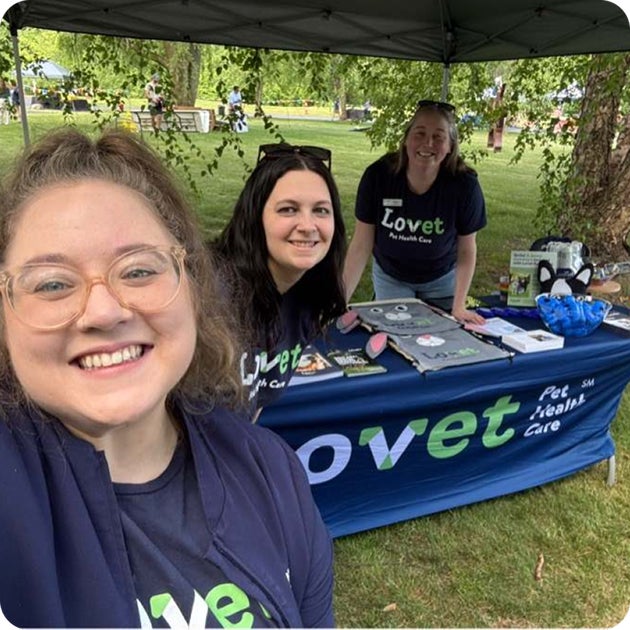 Three smiling Lovet staff members gather under a canopy at a branded table during the Humane Society of West Michigan birthday party event.
