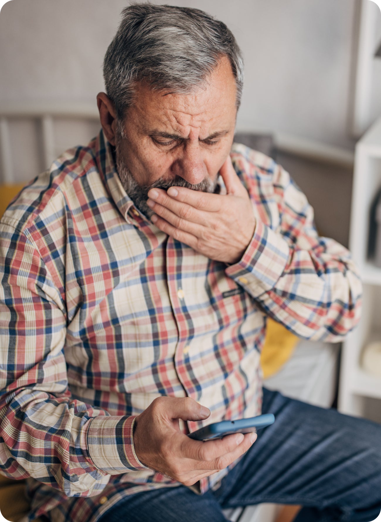 Man covering his mouth while looking at his phone, suggesting concern about what to do after a dental filling falls out before he can see a dentist.