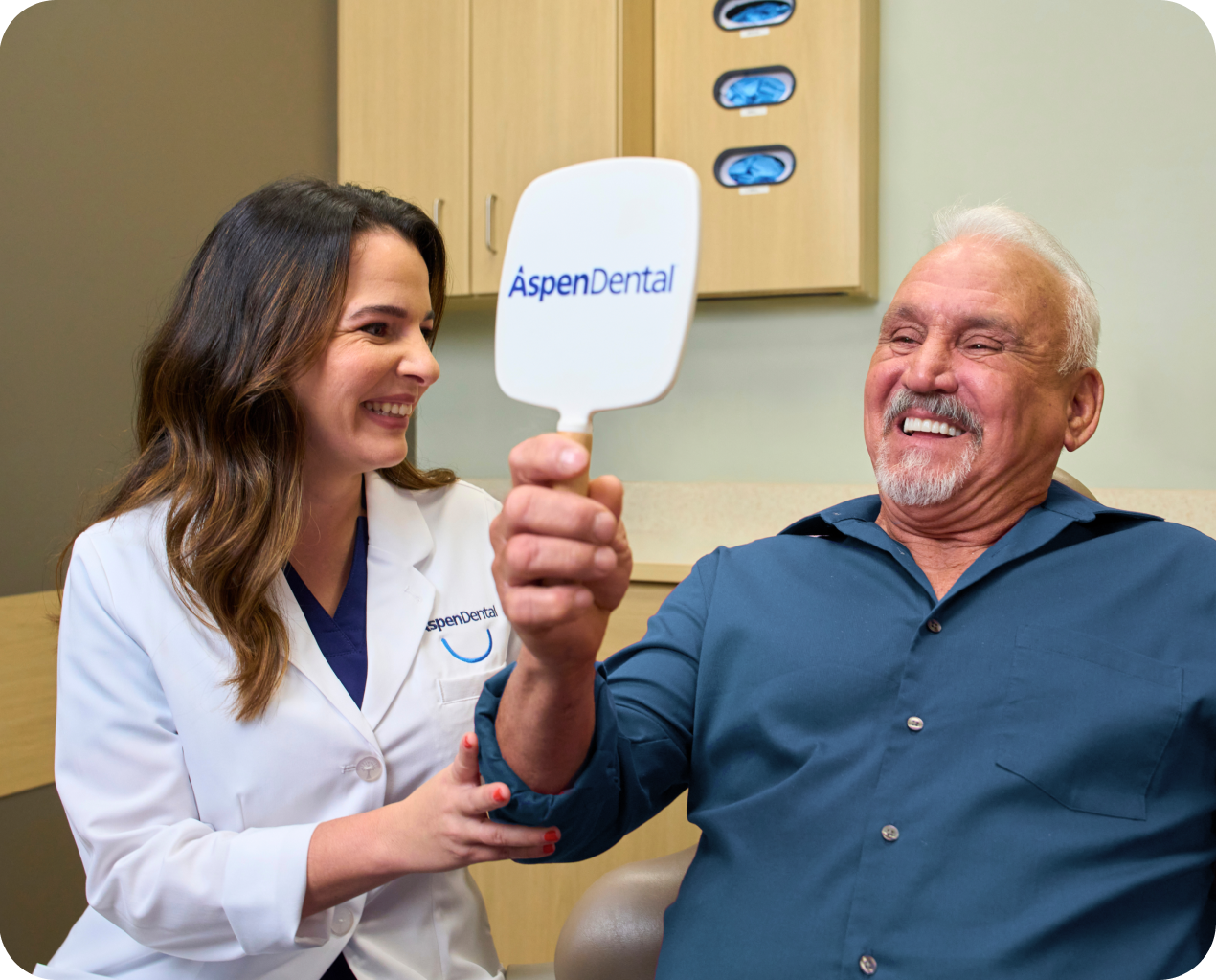 A dental professional and a smiling male patient holding an Aspen Dental mirror, celebrating successful dental treatment and patient satisfaction.