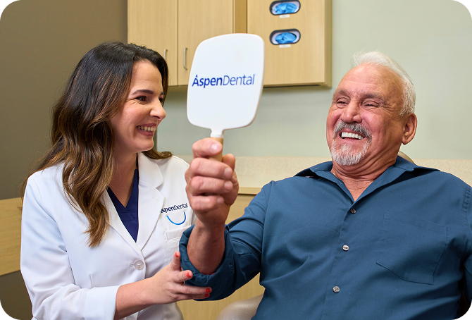 A dental professional and a smiling male patient holding an Aspen Dental mirror, celebrating successful dental treatment and patient satisfaction.