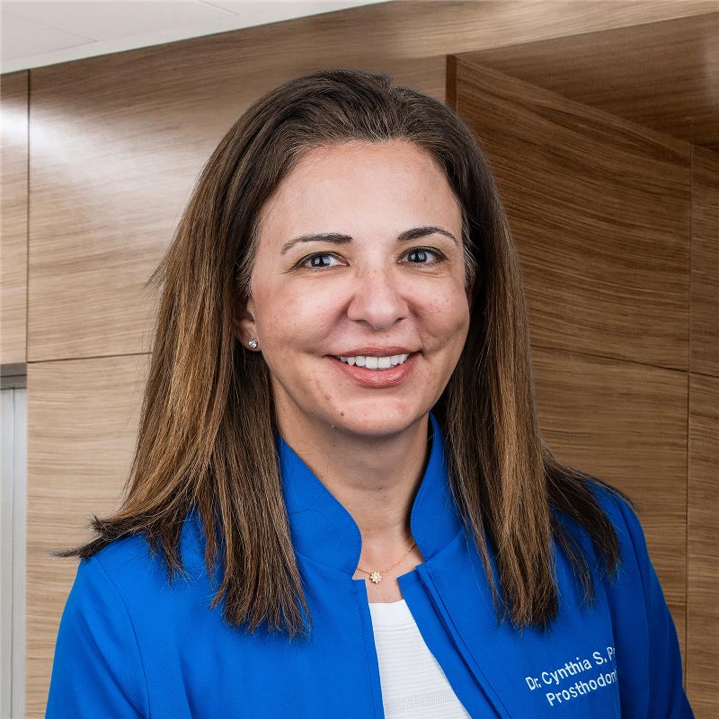 Dr. Cynthia Petrie smiling in front of a brown wood office wall