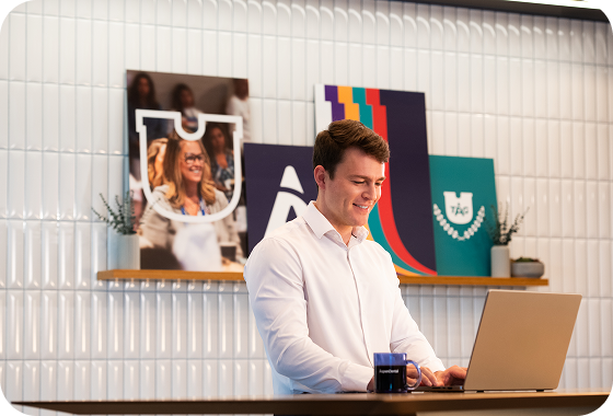 An Aspen Dental team member works on a laptop in a modern office space, with branded wall art and decor visible in the background.