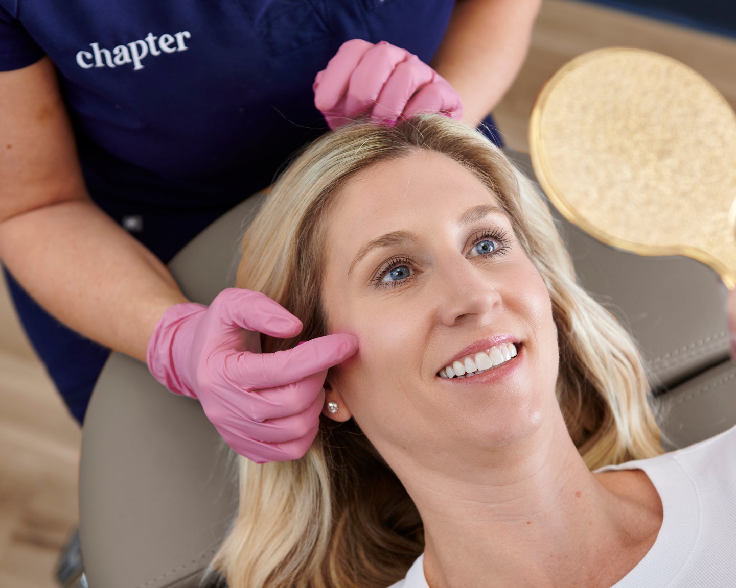 Woman smiling in a treatment chair while a Chapter Aesthetic Studio provider highlights facial areas, showcasing the benefits of filler for added volume and a refreshed look.