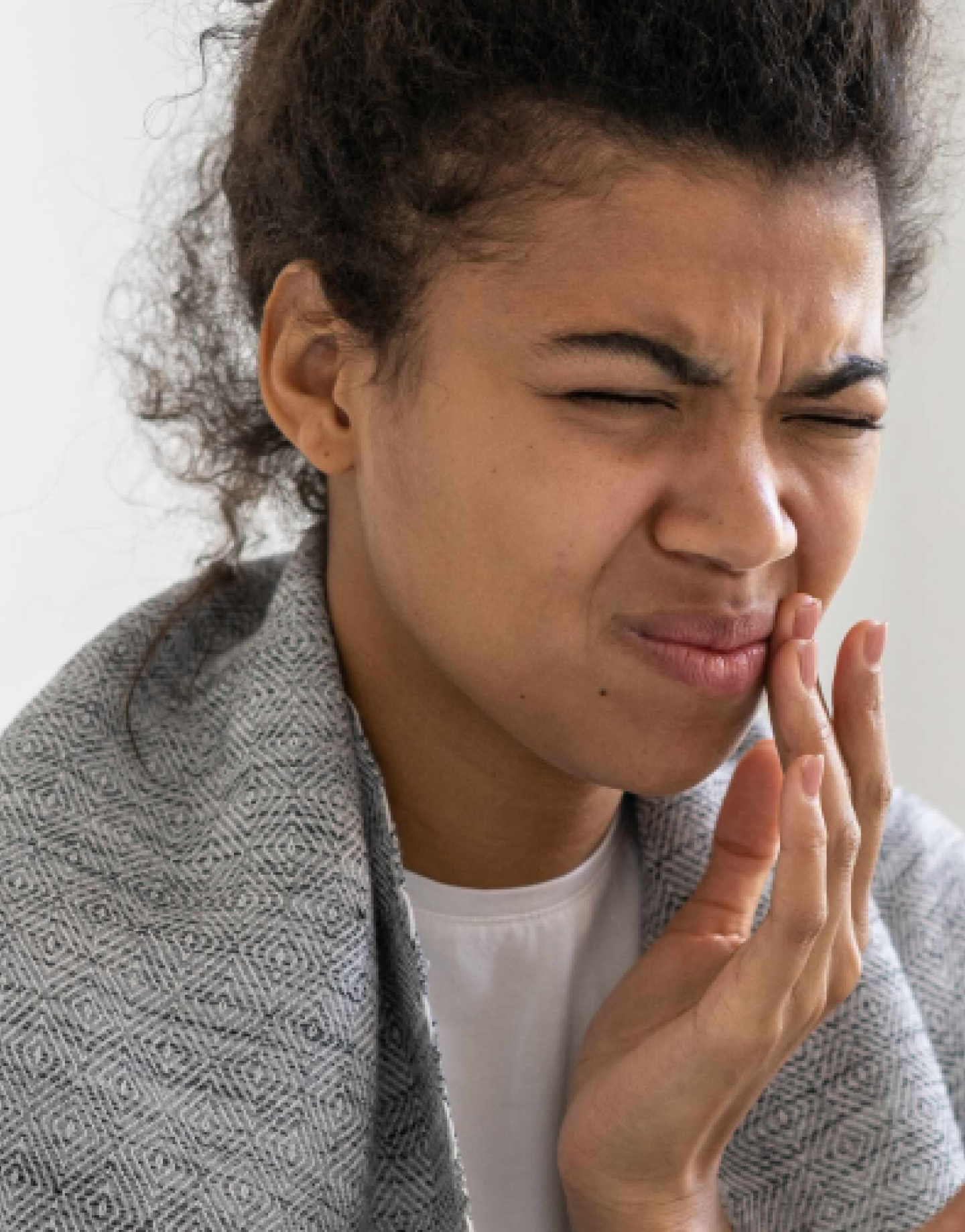 A young woman with a pained expression clutches her jaw, indicating a toothache.