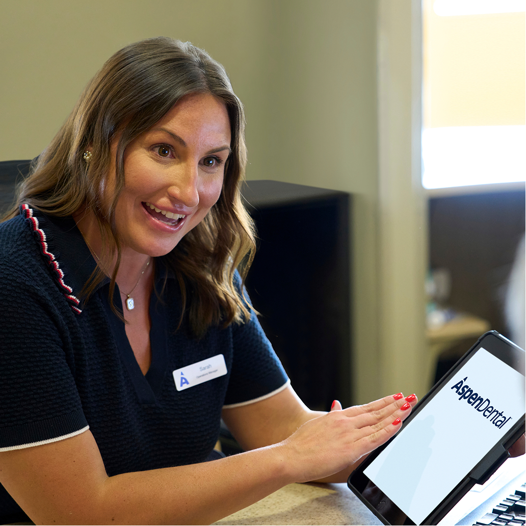 An Aspen Dental team member smiles while reviewing information on a tablet with a patient, explaining treatment or payment options during a consultation.