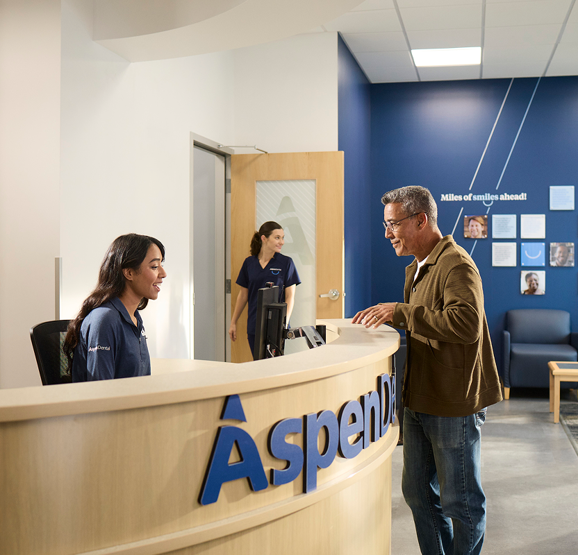 Patient speaking with a front desk team member at an Aspen Dental office reception area.
