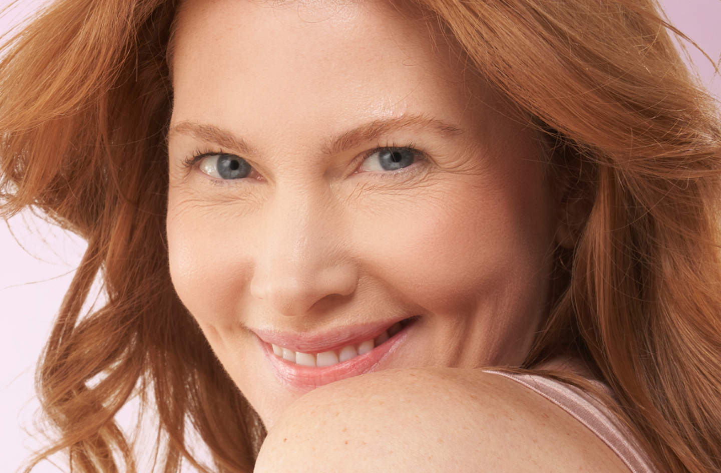 A woman with red hair is smiling and looking over her shoulder