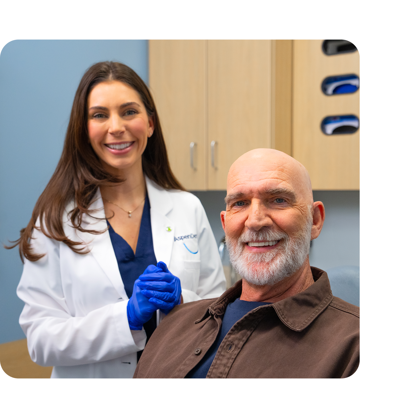 Male patient smiling while seated in a dental chair with an Aspen Dental dentist standing beside him, both smiling at the camera.