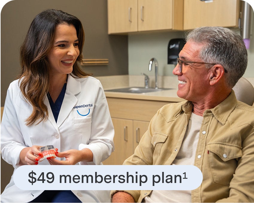 A dental professional in an Aspen Dental white coat speaking with an older patient in a dental office, with text reading "$49 membership plan²"