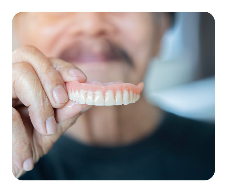 Older patient holds up a full upper denture, showing its natural look and gum-colored acrylic base.