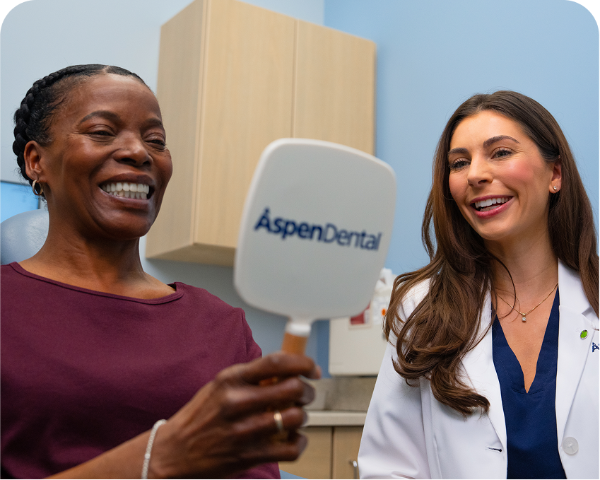 Patient smiling while holding an Aspen Dental mirror and talking with a dentist during an appointment.