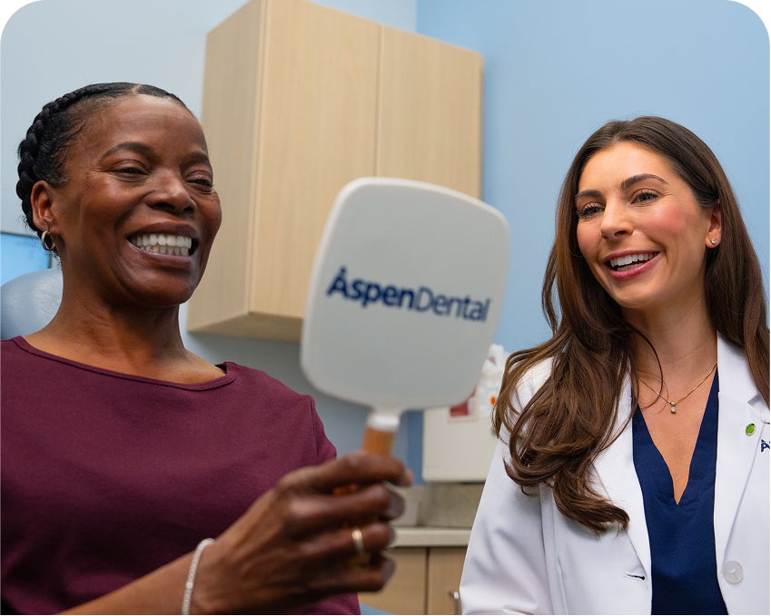 Patient smiling while holding an Aspen Dental mirror and talking with a dentist during an appointment.