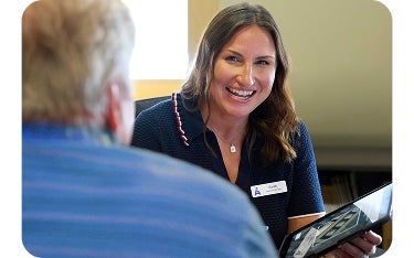 An Aspen Dental team member smiles warmly while speaking with a patient across the desk, holding a tablet during a consultation.