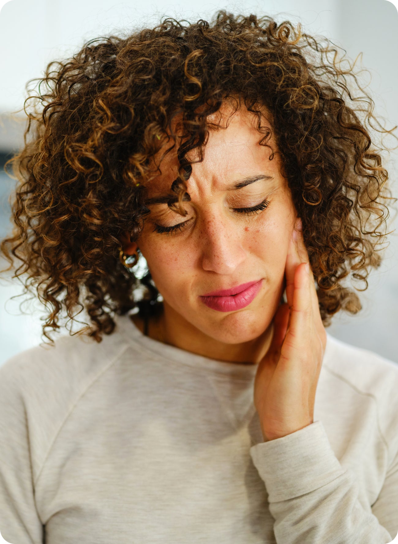 Woman holding her cheek with a pained expression, suggesting lingering tooth pain after a filling.