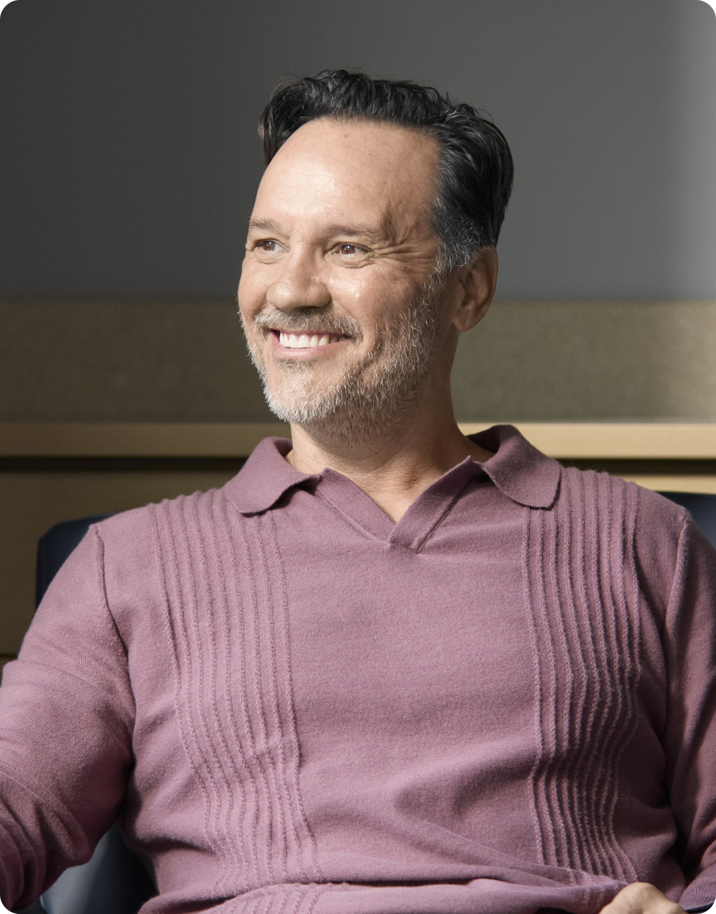 Smiling middle-aged man sitting indoors, showing bright, even teeth consistent with porcelain veneers.