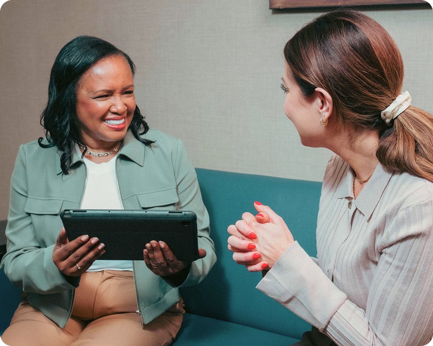 A ClearChoice care coordinator holding a tablet smiles while speaking with a patient seated beside her, illustrating a supportive dental consultation and personalized treatment discussion.