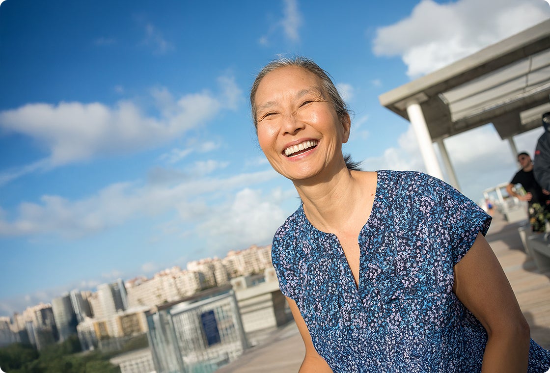A senior female patient in a navy blue floral top smiling confidently as she enjoys the outdoors.