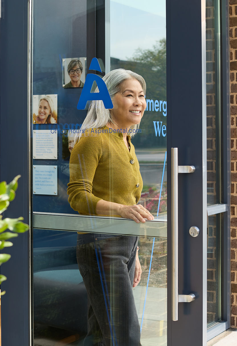 Smiling older woman leaving an Aspen Dental office through a glass door.