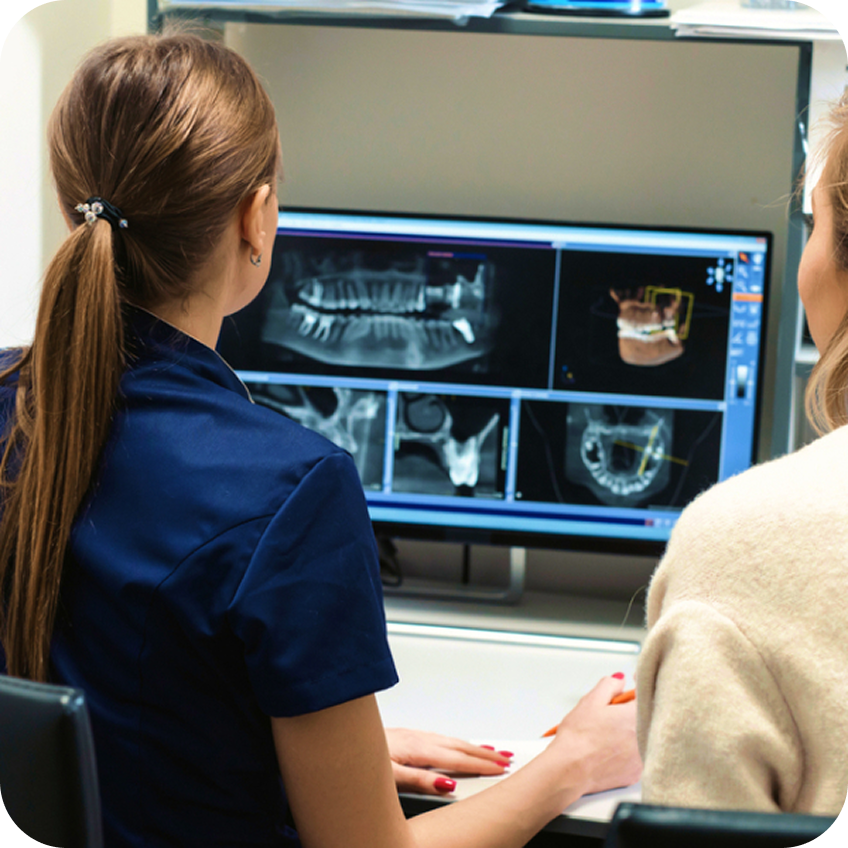 Two Aspen Dental team members sit side by side reviewing detailed dental X-rays and 3D imaging on a computer monitor during a treatment planning discussion.