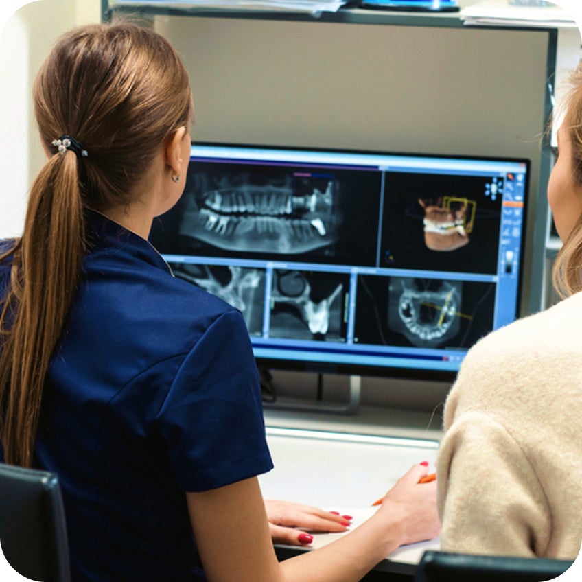 Two Aspen Dental team members sit side by side reviewing detailed dental X-rays and 3D imaging on a computer monitor during a treatment planning discussion.