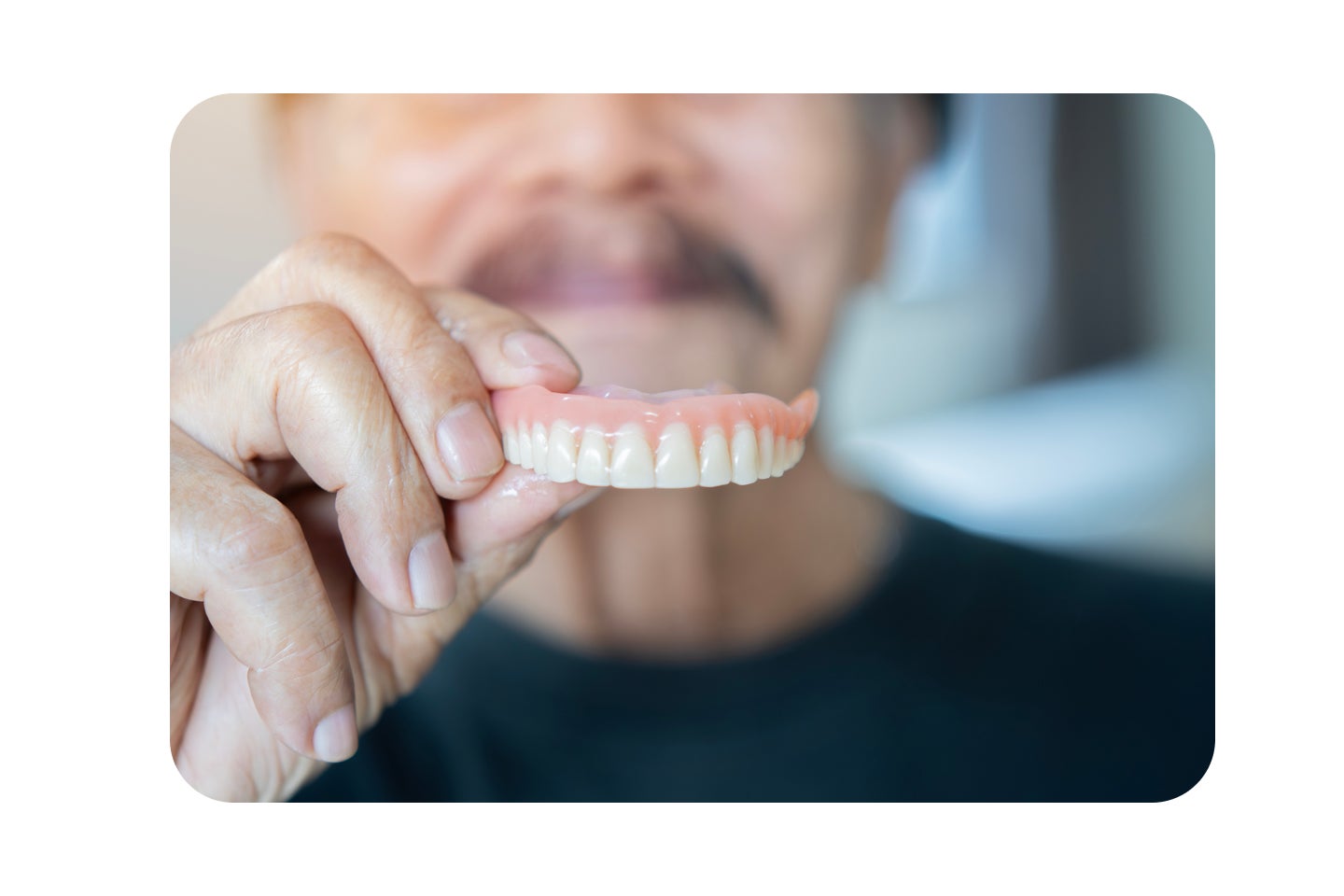 Older patient holds up a full upper denture, showing its natural look and gum-colored acrylic base.