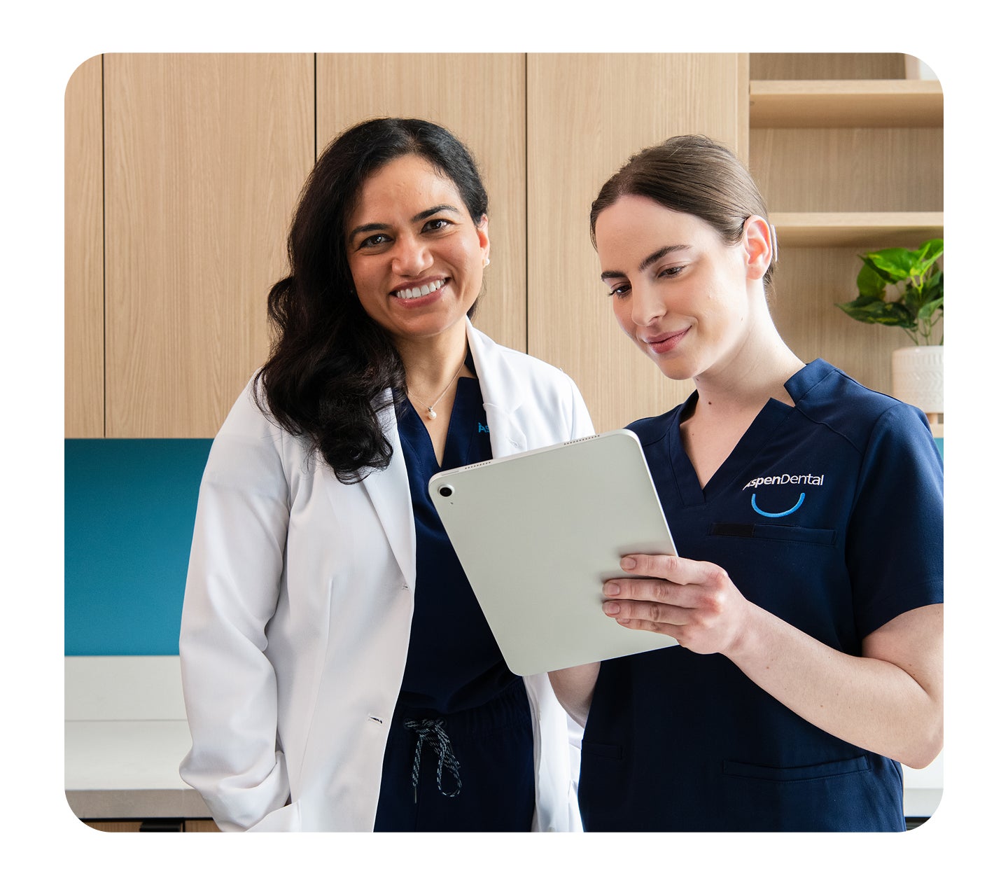 Two Aspen Dental team members stand together in a modern office, smiling while reviewing information on a tablet.