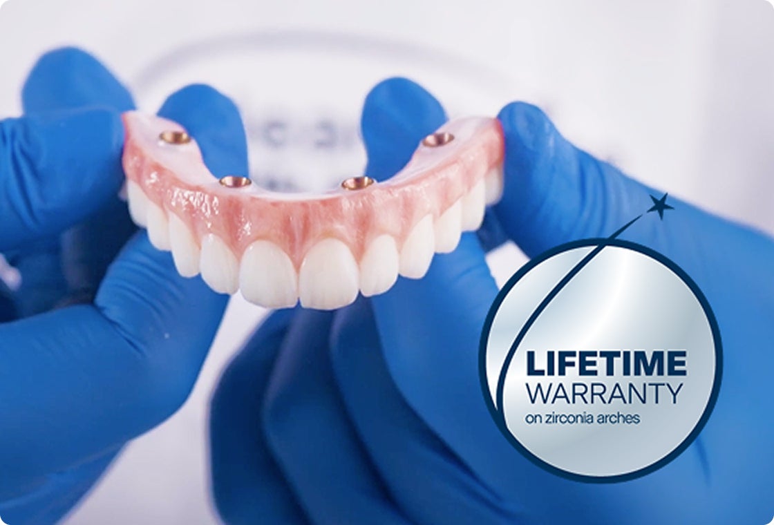 Gloved hands hold a zirconia full arch restoration, highlighting the durability of ClearChoice dental implants with a visible “Lifetime Warranty on zirconia arches” badge.
