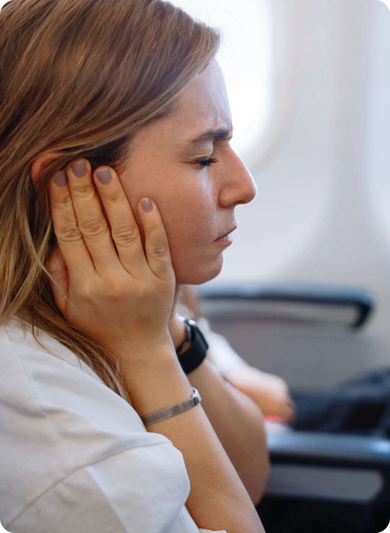 Woman sitting on an airplane holding her jaw in discomfort, suggesting barodontalgia or flyer's toothache during air travel.