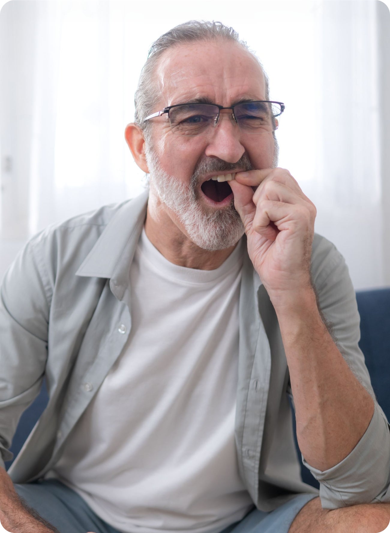 Older man touching a painful tooth at home, illustrating a common mistake to avoid during a dental emergency.